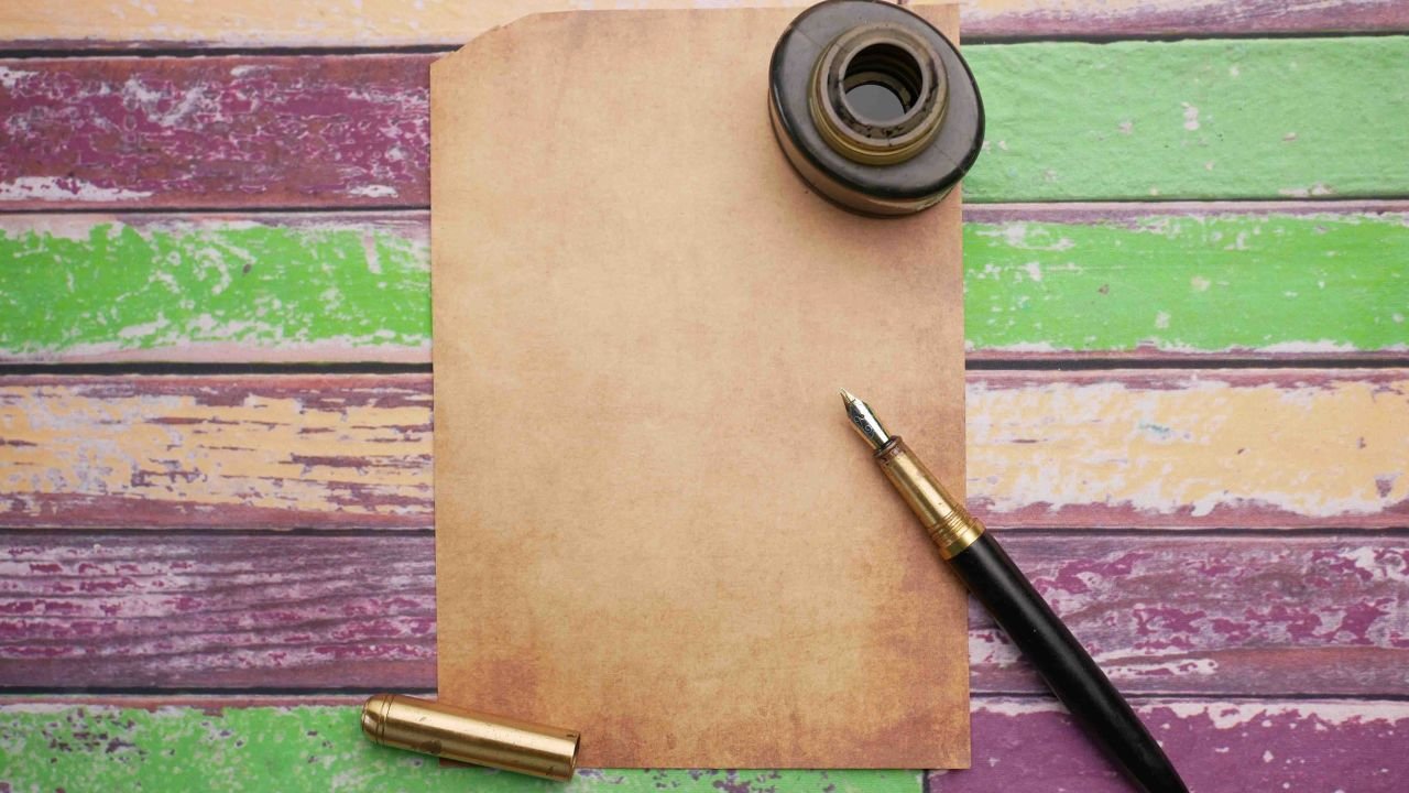 Flat lay of vintage paper with ink bottle and pen on a colorful wooden surface.