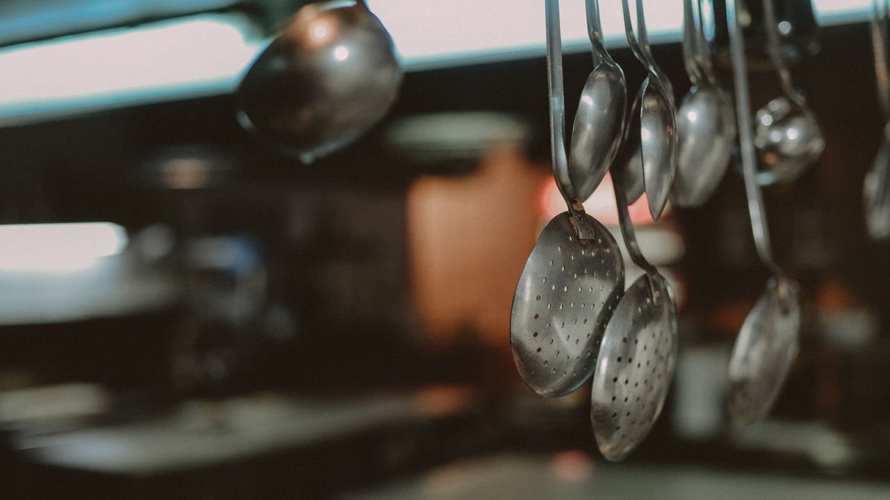 Close-up of hanging metal spoons and ladles in a kitchen, blurred background