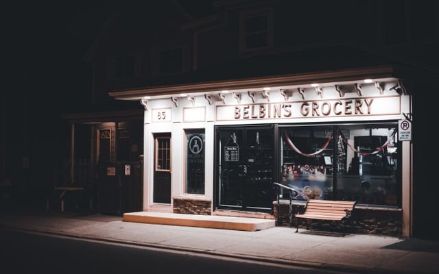 Nighttime view of Belbin's Grocery storefront with warm lighting and an inviting bench.