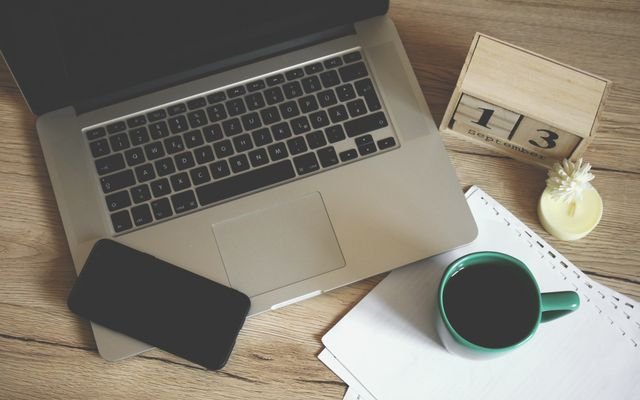 Modern office desk setup with laptop, smartphone, coffee, and calendar for productive work environment.