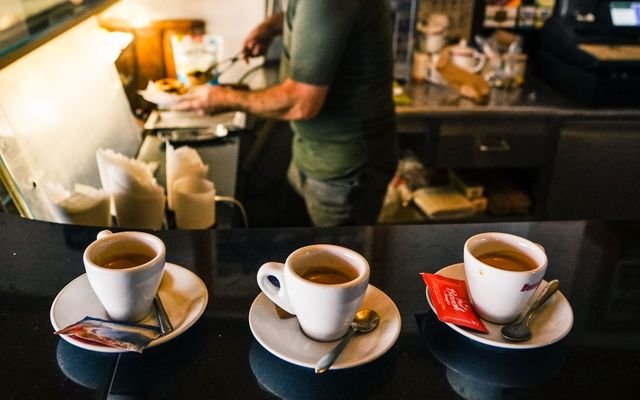 A barista in a café preparing espresso drinks on a countertop with three coffee cups in focus.