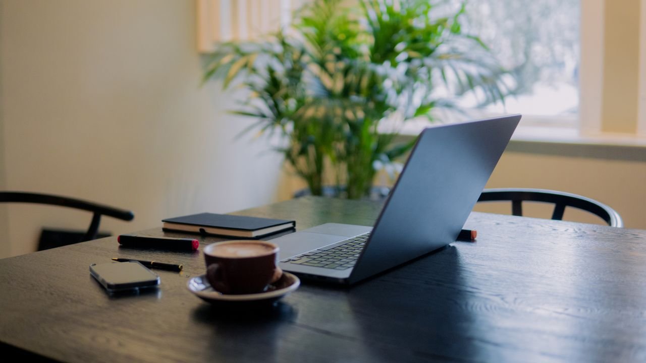 A warm, inviting workspace in Amsterdam featuring a laptop, coffee, and potted plant.