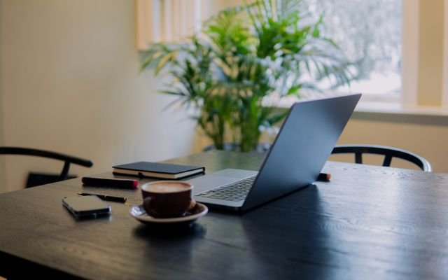 A warm, inviting workspace in Amsterdam featuring a laptop, coffee, and potted plant.