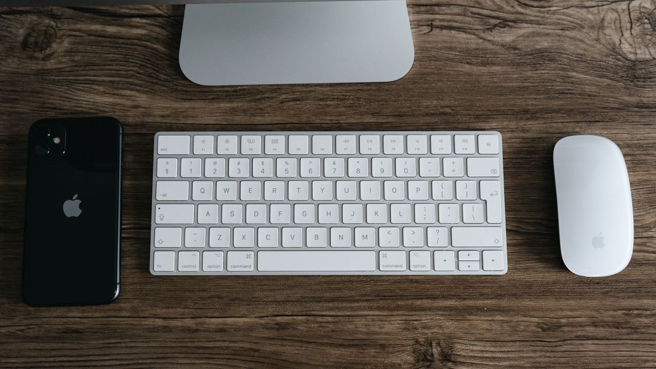 A minimalist workspace featuring a smartphone, keyboard, and mouse on a wooden desk.