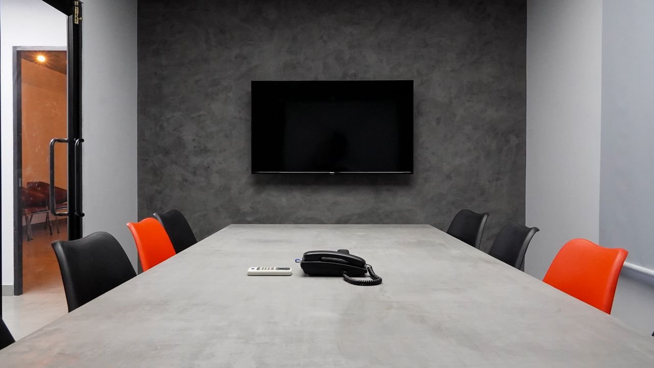 Sleek conference room featuring a large table, black and red chairs, and a wall-mounted TV.