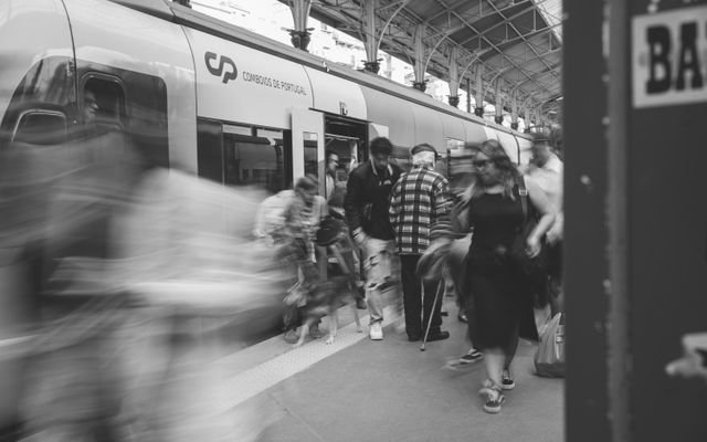 A black and white scene of commuters at a Lisbon train station, showcasing urban movement.