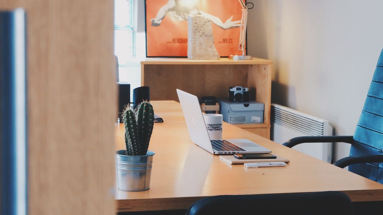 A modern office desk setup featuring a cactus plant, laptop, and stylish decor in a contemporary office space.