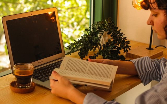 Warm indoor setting with a laptop, coffee, and book creating a cozy workspace.