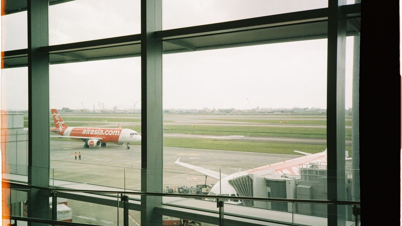 View of an AirAsia plane taxiing on the runway from inside the airport terminal.