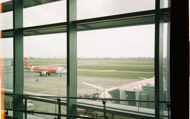 View of an AirAsia plane taxiing on the runway from inside the airport terminal.