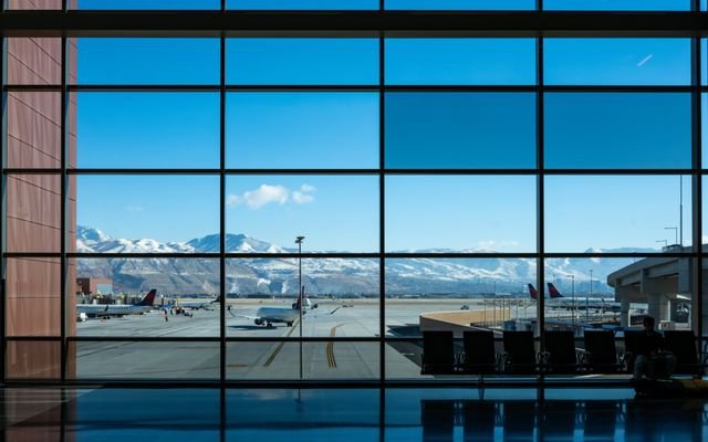 Panoramic view of airport terminal and runway with snow-capped mountains in the background.