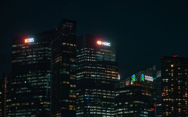 Illuminated city skyscrapers of major banks in Singapore's financial district at night.