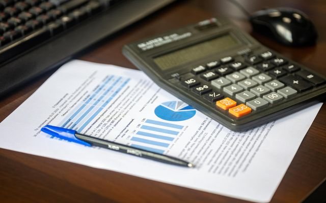 Desk with calculator, financial report, and pen, suggesting business analysis.
