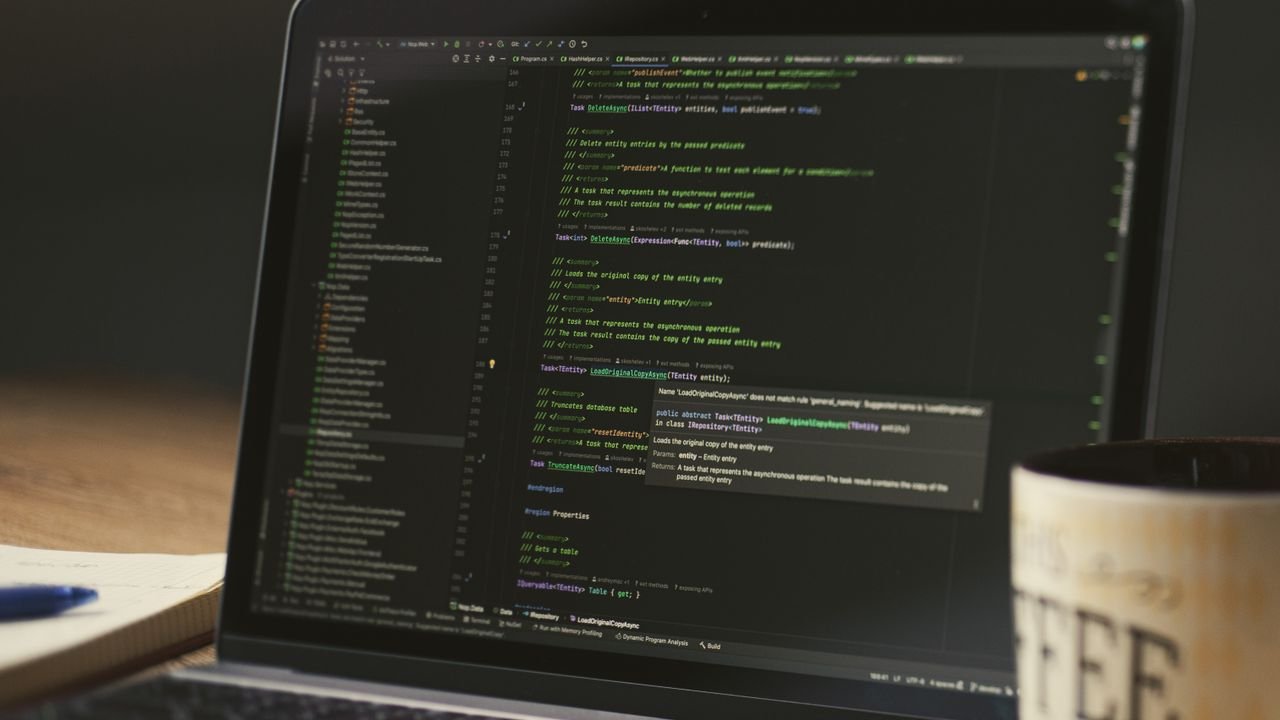 A close-up of a laptop displaying code in a dimly lit room with a coffee mug nearby.