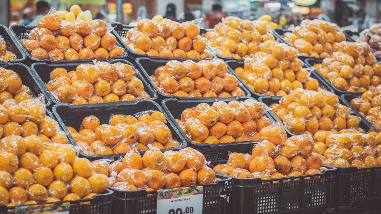 Stack of fresh oranges wrapped in plastic at a grocery store, priced with tags.