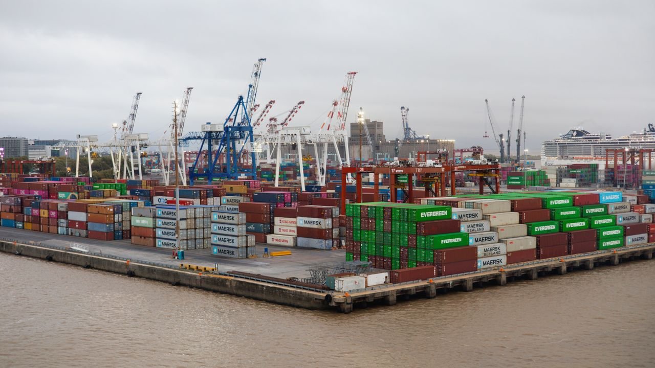 A bustling shipping port with stacked cargo containers and cranes under overcast skies.