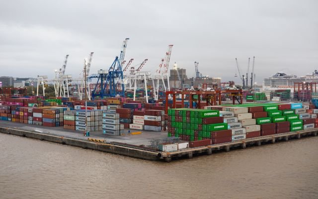 A bustling shipping port with stacked cargo containers and cranes under overcast skies.