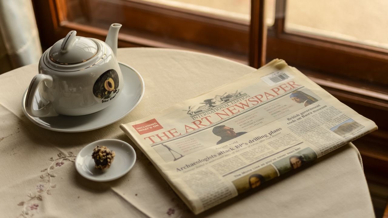 A serene indoor scene with a teapot, a newspaper, and a chocolate treat by the window.