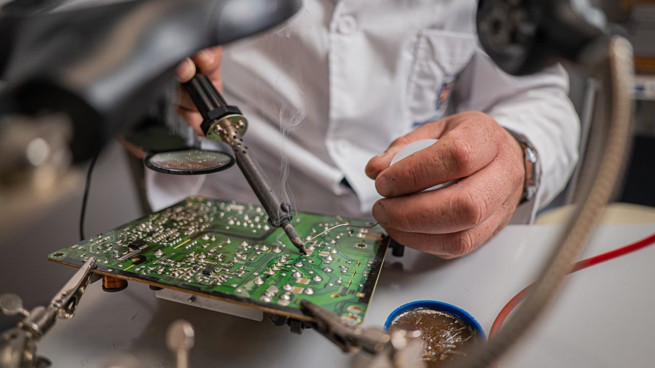 Close-up of technician using soldering iron on a circuit board in a lab setting.