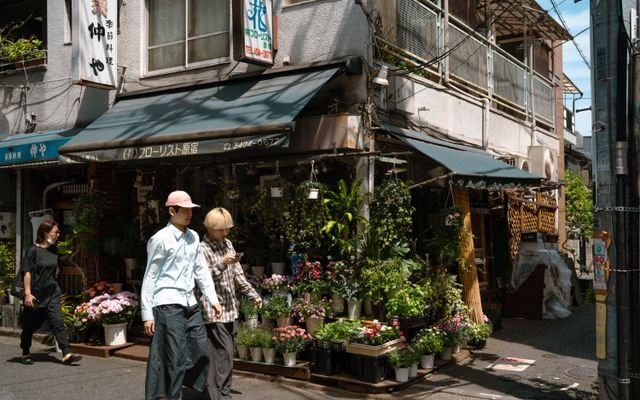 Charming florist shop in Tokyo's streets with pedestrians passing by, captured in daylight.
