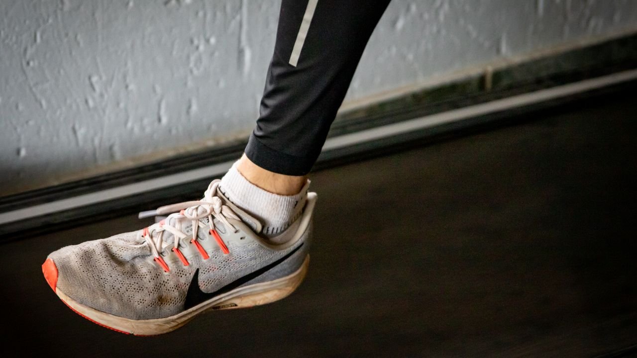 A detailed view of a sneaker mid-stride on a treadmill, showcasing active lifestyle footwear.