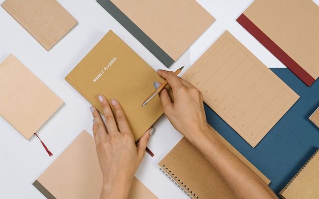 Organized flat lay of stationery items with hands writing in a planner, suitable for productivity themes.