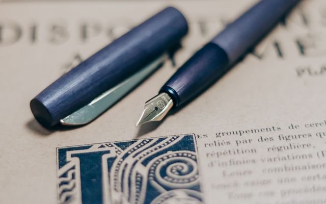 A close-up shot of a navy blue fountain pen on a vintage book page, showcasing elegant writing tools.