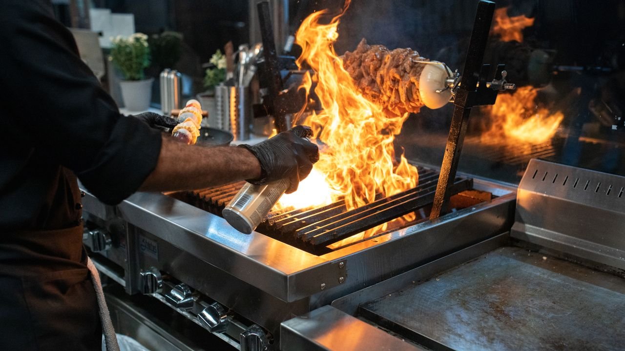 Chef grilling meat with spectacular flames in a modern kitchen setup.