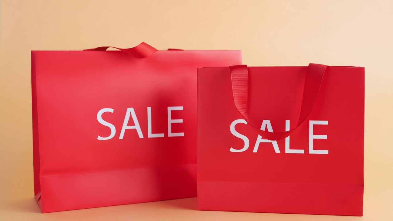 Bright red shopping bags on a neutral background with a sale text, perfect for marketing promotions.