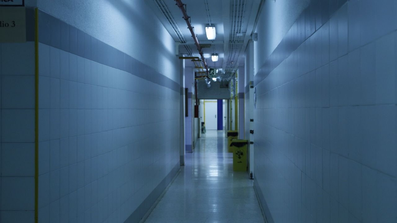 A deserted, dimly lit hallway with tiled walls and overhead lights.
