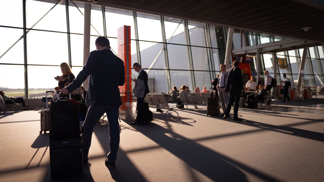 Travelers in a bustling airport terminal with carry-on luggage waiting for departure.