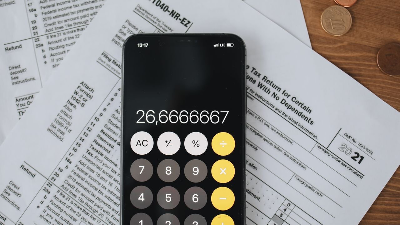 Smartphone calculator over tax forms with coins, symbolizing tax calculation and finance.