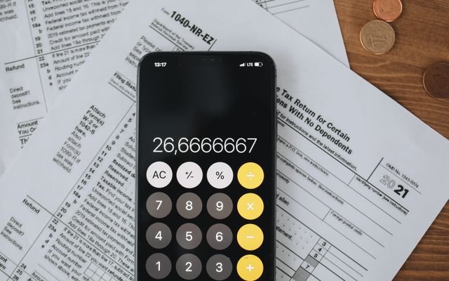 Smartphone calculator over tax forms with coins, symbolizing tax calculation and finance.
