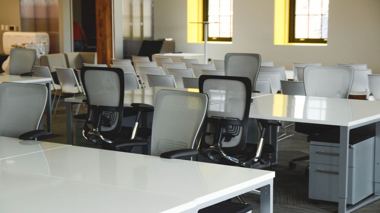 Spacious open office workspace with desks, chairs, and natural lighting.