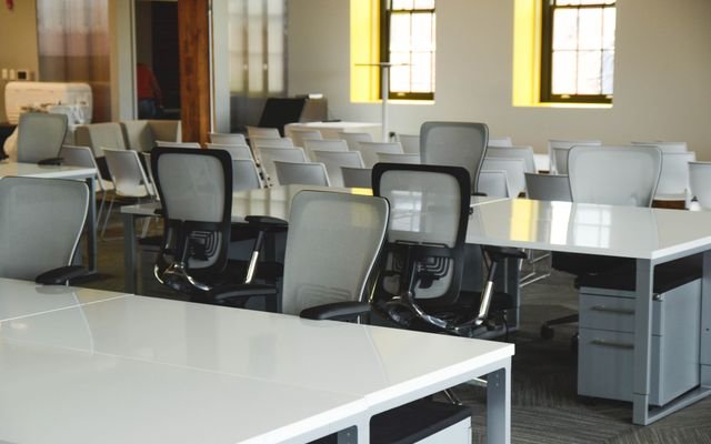 Spacious open office workspace with desks, chairs, and natural lighting.