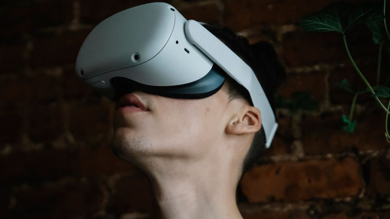 Young male wearing modern goggles of virtual reality and immersing in cyberspace while being in room with brick walls