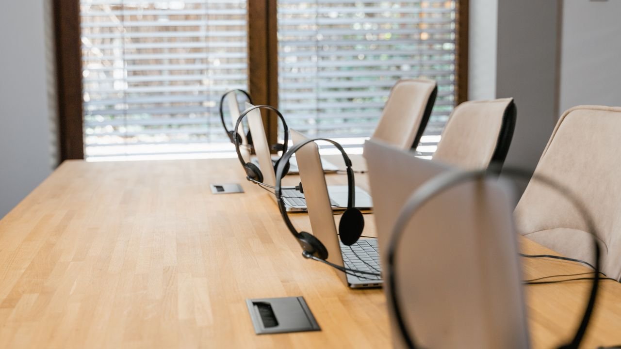 Empty office workspace featuring laptops with headsets, ready for a productive day.