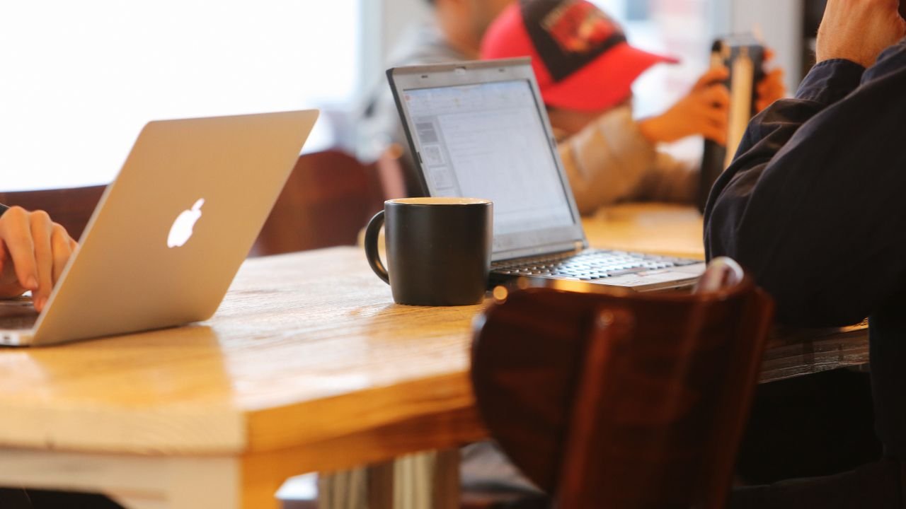 Group working in a cozy cafe with laptops and coffee mugs on a shared table.