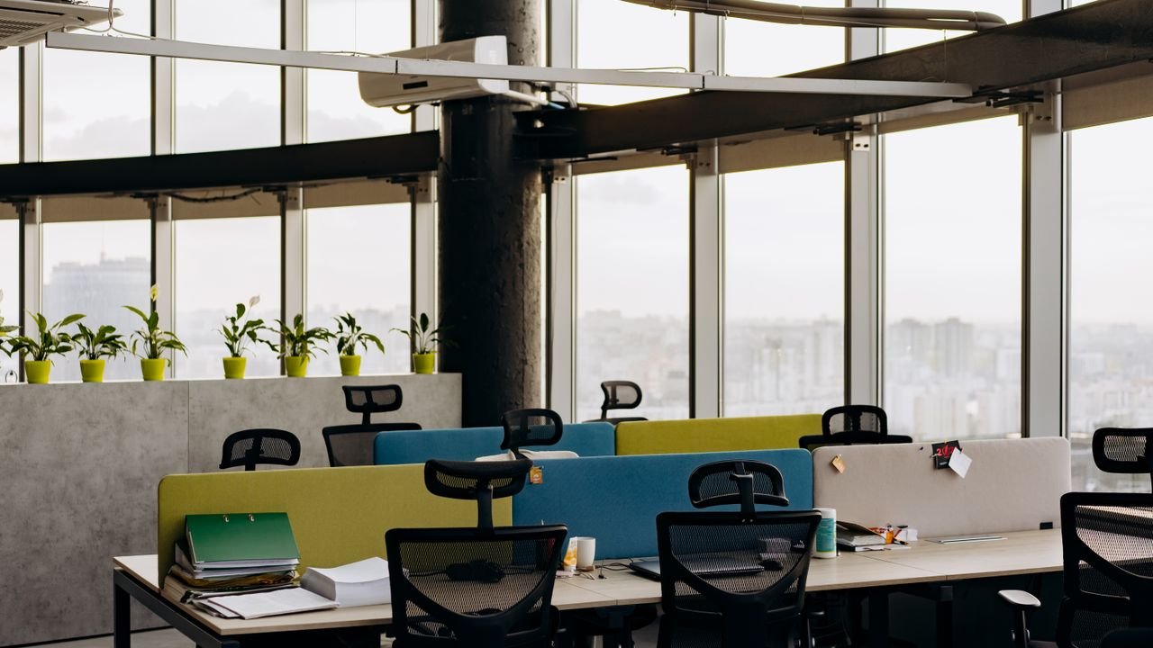 A spacious open office with colorful dividers, large windows, and a cityscape view, perfect for creative work environments.