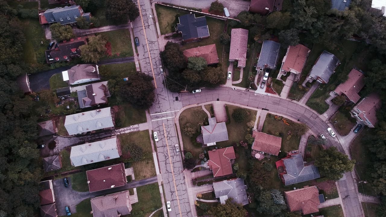 Drone shot capturing suburban neighborhood streets and houses from above.