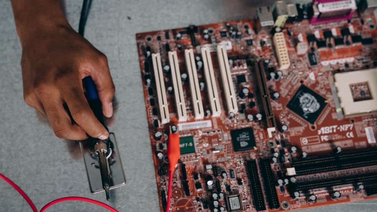 An engineer uses a soldering tool on a motherboard, showcasing technology and precision.