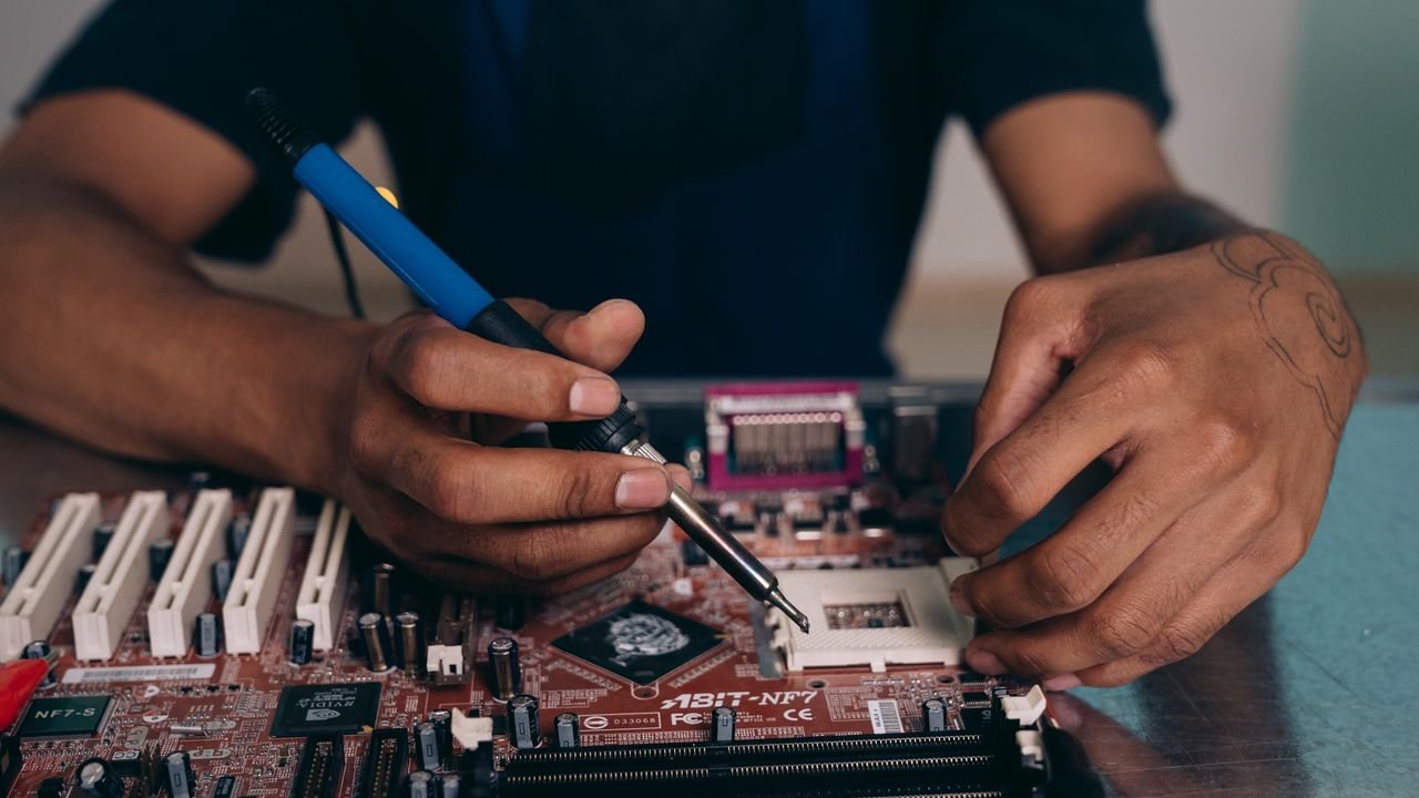 Engineer skillfully soldering components on a motherboard in a tech workshop.
