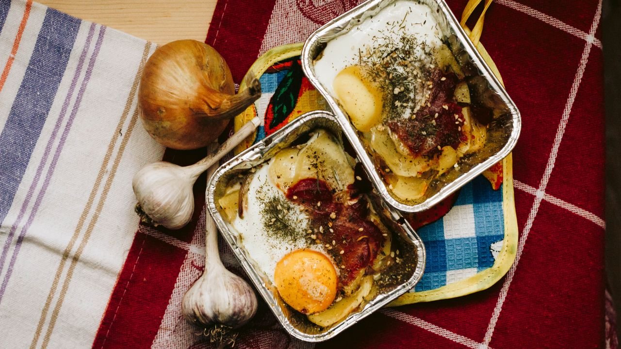 Delicious baked egg dish with vegetables in aluminum trays on a colorful tablecloth.