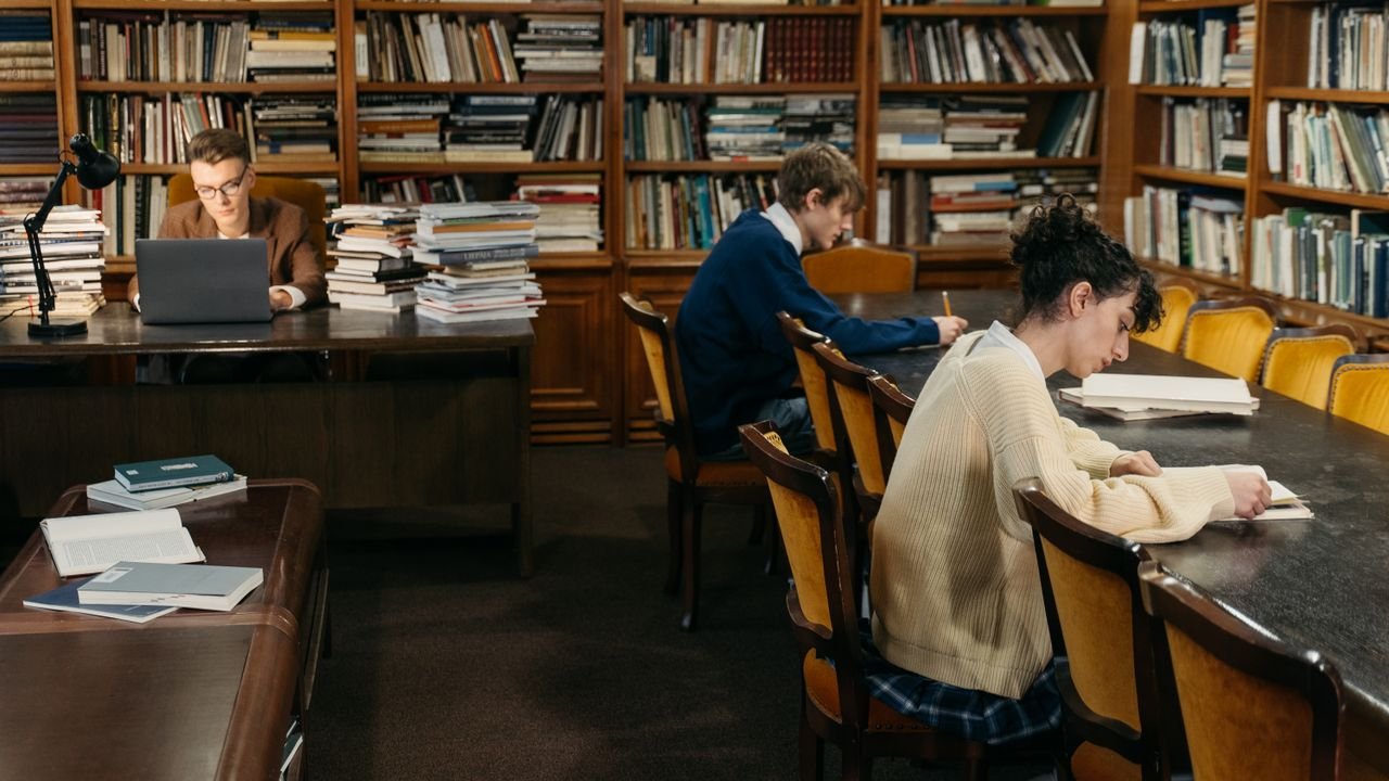 Students engaged in study inside a peaceful library with bookshelves.