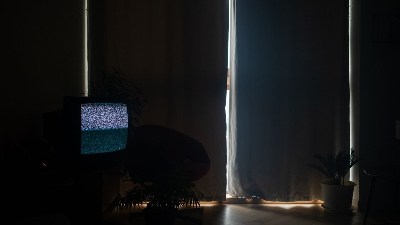 A dimly lit living room with static on the TV and curtains drawn, creating a moody atmosphere.