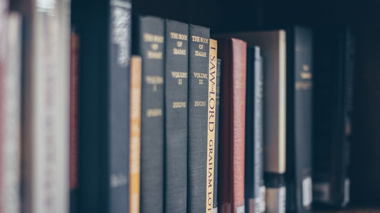 A focused view of books on a library shelf featuring various titles in soft lighting.